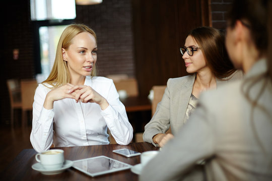 Blond-haired white collar worker sharing ideas with her colleagues while having informal meeting in cozy coffeehouse