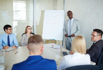 Multi-ethnic team of talented managers discussing growth strategy of their company while sitting in modern board room