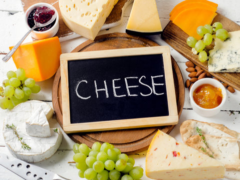 Assorted cheeses served with grapes, jam,  bread and nuts on wooden background
