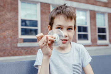 boy holds a fidget spinner in his hand. Spinning spinner and face of kid closeup on a schoolyard....
