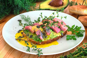 Sandwich with herring, avocado and egg yolk. Wooden background. Close-up. Top view