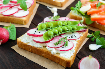 Several kinds of sandwiches with vegetables: radish, tomatoes, cucumber, arugula on crispy toast on a dark wooden background. Vegetarian dish. Proper nutrition. Healthy food. Breakfast.