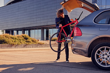 A man puts fixed bicycle in the car's trunk.
