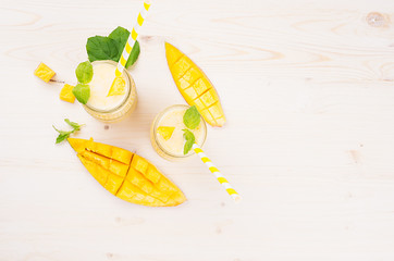 Freshly blended yellow mango fruit smoothie in glass jars with straw, mint leaves, mango slices,...