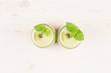 Freshly blended green kiwi fruit smoothie in glass jars with straw, mint leaf, top view. White wooden board background, copy space.