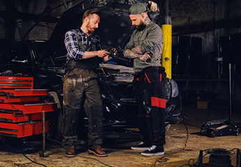 Two bearded  mechanics inspecting car's engine parts.