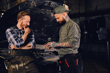 Two bearded  mechanics inspecting car's engine parts.