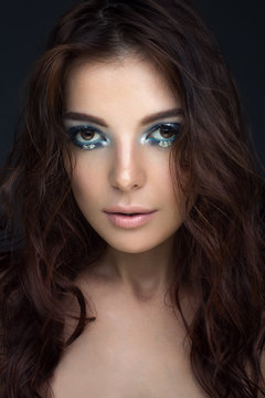 Close-up portrait of girl with dark hair with blue eyeshadow and silver dots, looking at the camera