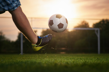 Soccer player kicking a ball in to the goal, sunset in the background - obrazy, fototapety, plakaty