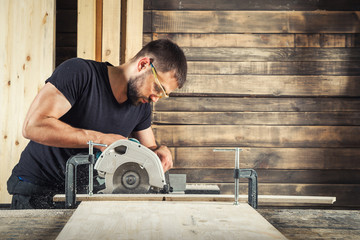 The man builder uses a modern circular   saw in order to saw the board in the workshop