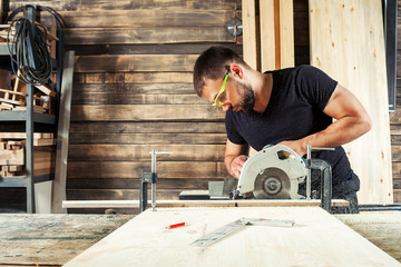 The man builder uses a modern circular   saw in order to saw the board in the workshop