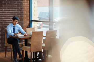 Concentrated bearded entrepreneur taking necessary notes while sitting in cozy cafe with panoramic...