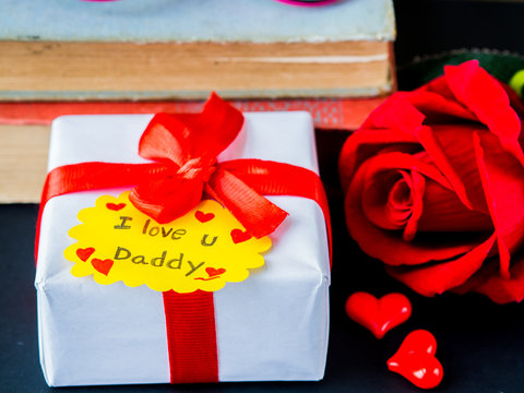 Father's day concept. I LOVE YOU DADY message with red rose, two red heart and gift on pink background
