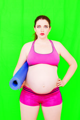 Pregnancy Yoga Fitness concept. Portrait of young pregnant yoga model posing with sports mat on the green background