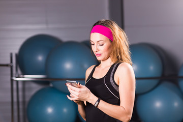 Fototapeta premium sport, fitness, technology and people concept - young woman with activity tracker and smartphone in gym