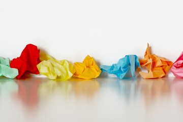 Line of colorful crumpled paper on a white table with reflection against a white background