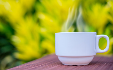 Coffee cup on old wooden table with smoke on blur yellow leaf background. Food and Drink.