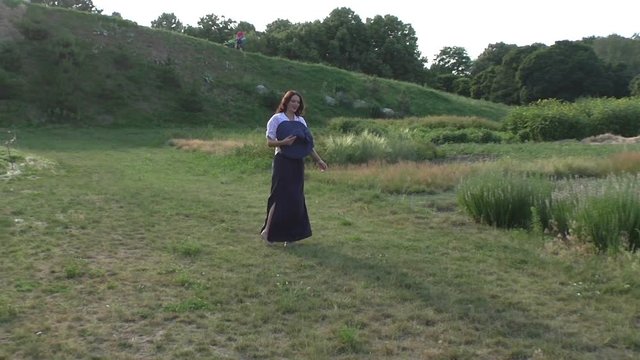 Woman in a big hat is walking along the grass in a meadow, she is happy.