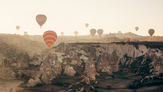 Colorful air balloons flying over Cappadocia landscape at sunrise