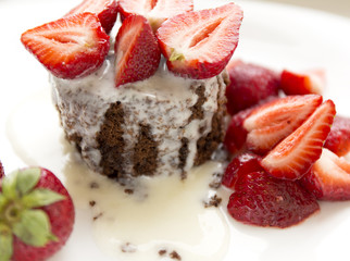 Delicious homemade chocolate cake with fresh red strawberries and cream sauce on white plate.