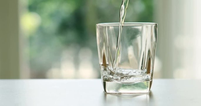 pouring the fresh water drink into the glass on the table in the living room with nature green background