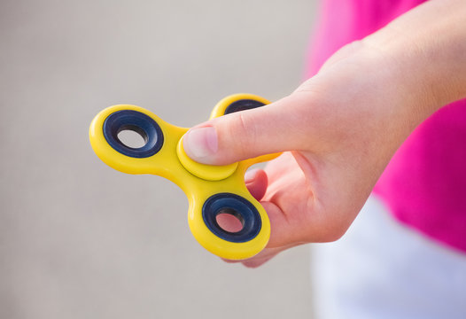 Little girl is playing a yellow spinner in her hand outdoors.