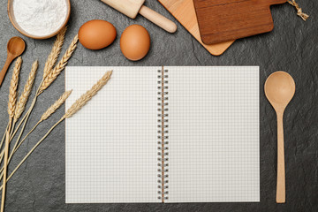 Top view kitchen utensils and baking ingredients mockup on dark border background  with notebook and pencil.