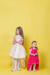 Fototapeta na wymiar Two sisters in dresses on a yellow background look in different directions and offended