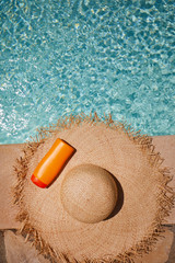 Hat and bottle of sun cream by the pool