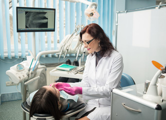 Female dentist with dental tools - mirror and probe checking up patient teeth at dental clinic...