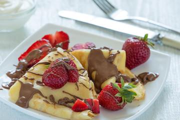 Pancakes with strawberries drizzled with chocolate. On a white wooden background.