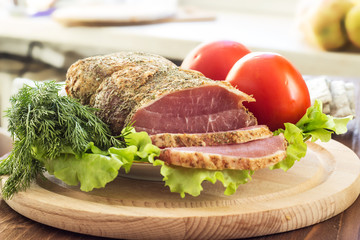 Slices of smoked meat with lettuce and tomato on a wooden board. Selective focus. Horizontal.