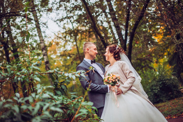 Bride and groom at wedding Day walking Outdoors on autumn nature. Bridal couple, Happy Newlywed woman and man embracing in green park. Loving wedding couple outdoor. Bride and groom