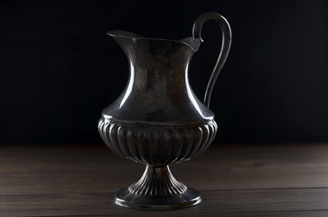 Fototapeta na wymiar Metal decoration jug on wooden table. Backlighting.