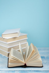 Book stacking. Open book, hardback books on wooden table and blue background. Back to school. Copy space for text.
