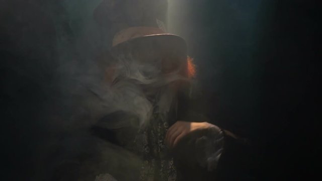 Cheerful Hatter sits in smoke