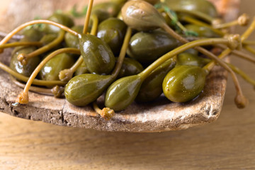 Canned capers in wooden dish .