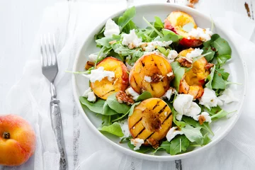 Fototapeten Fresh salad with grilled peach halves, arugula and burrata on a plate on white distressed wooden background. Top view. Summer food concept © Anastasiia Nurullina