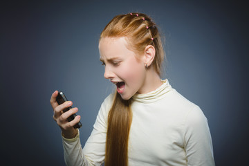 Angry redhead girl with cell phone. isolated on gray