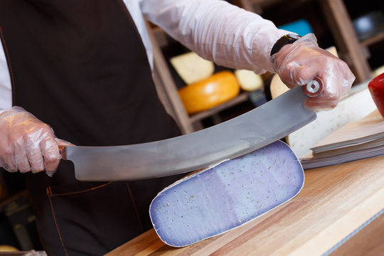 Cutting gouda pesto blue cheese in grocery shop