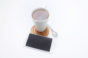 Fototapeta na wymiar White cup with tea on wooden stand with spoon and white phone on white background