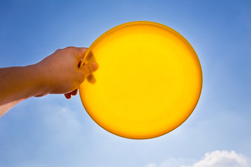 male hand catching holding yellow frisbee disc against blue sky background - obrazy, fototapety, plakaty