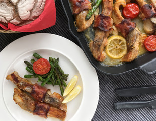 Fillets of carp grilled with bacon, garlic, lemon, asparagus and tomatoes. Top view.