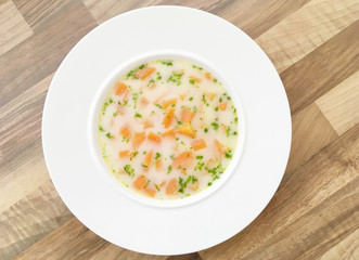 Vegetable carrot soup with cream and green herbs. Wooden background. Top view.