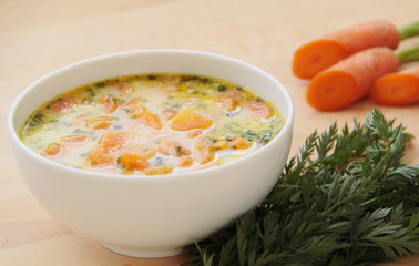 Vegetable carrot soup with cream and herbs. Ingredients around the bowl. Wooden table. Close up view.