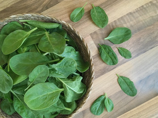 Fresh spinach leaves in a wicker basket. Wooden background. Top view.