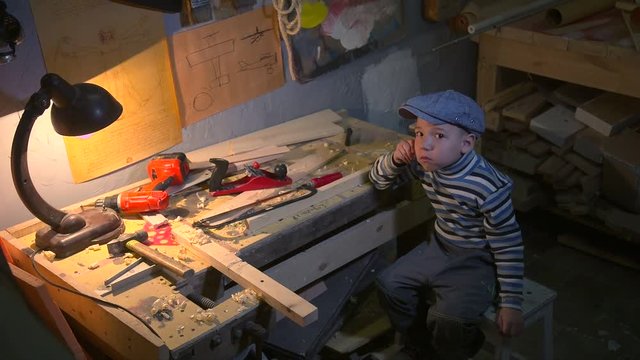 Cute boy sitting in carpenter workroom
