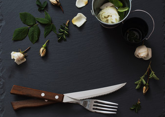 white roses and silverware on black stone background