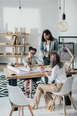 Multiethnic group of professional young architects working with blueprints in modern office
