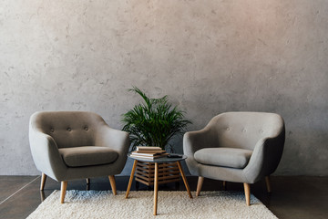 Two cozy grey armchairs standing on white carpet in empty room - obrazy, fototapety, plakaty